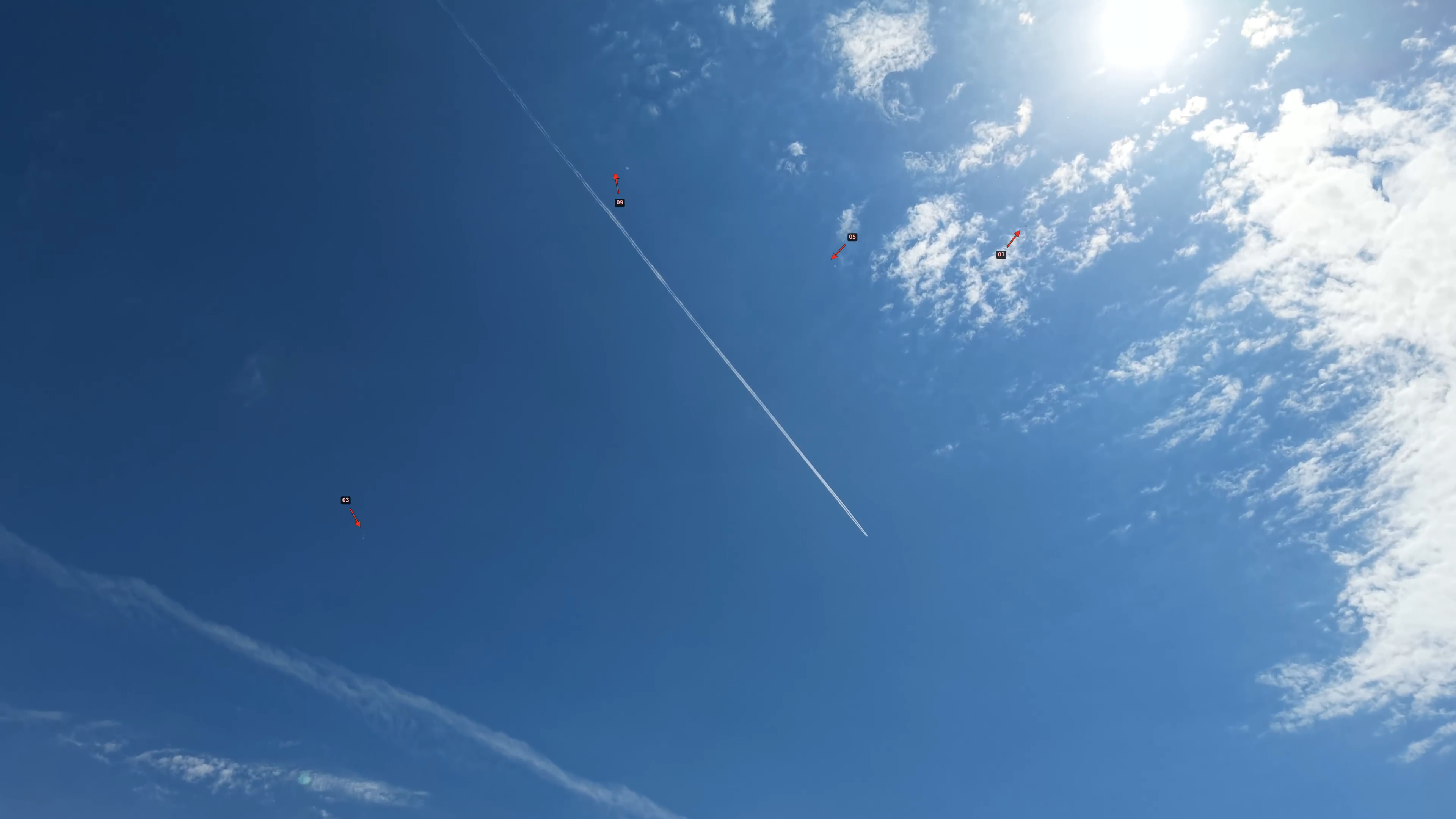 Wide drone frame showing contrail and four red arrows pointing at small objects
