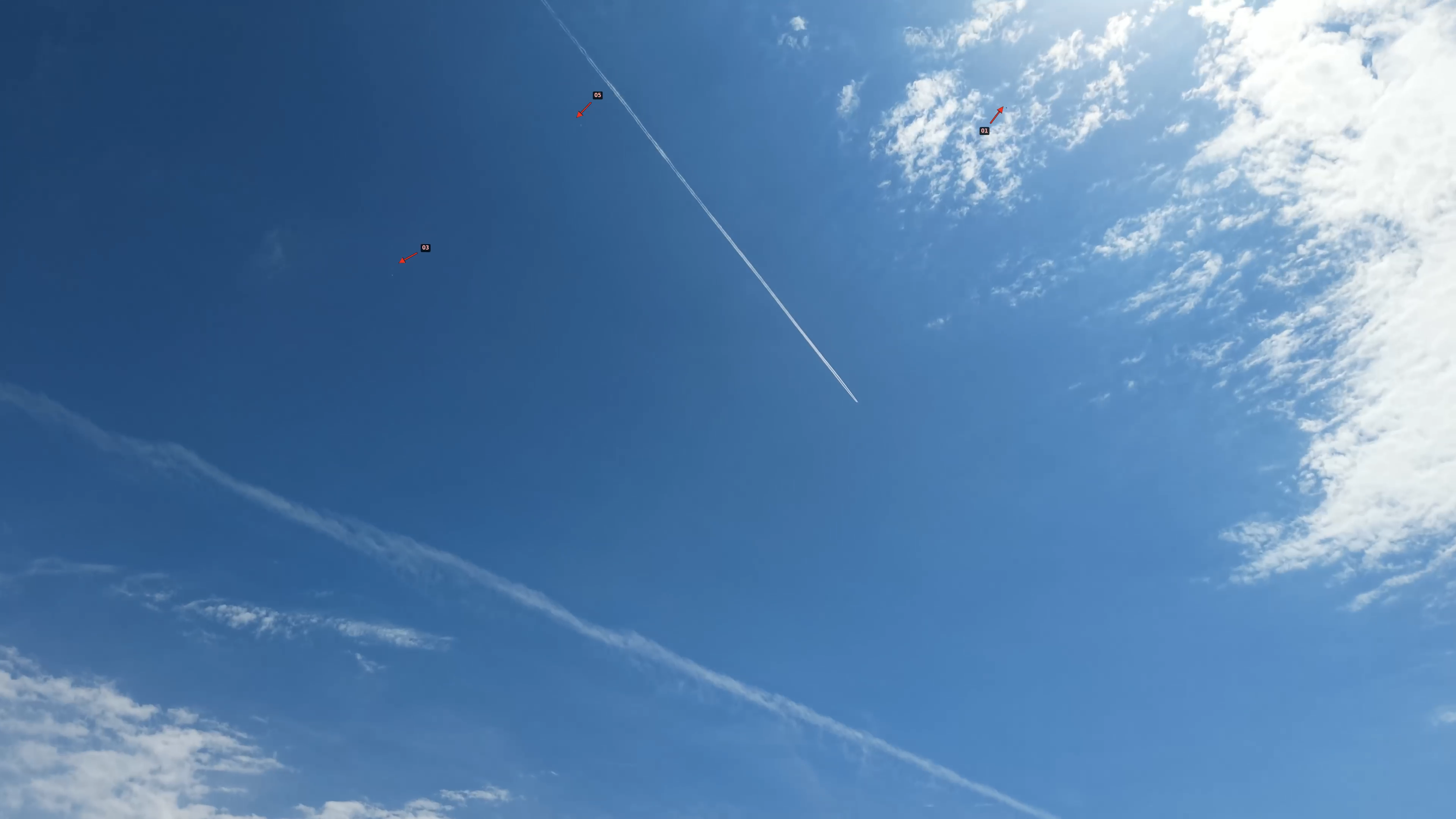 Drone frame with contrail and red arrows pointing at multiple objects